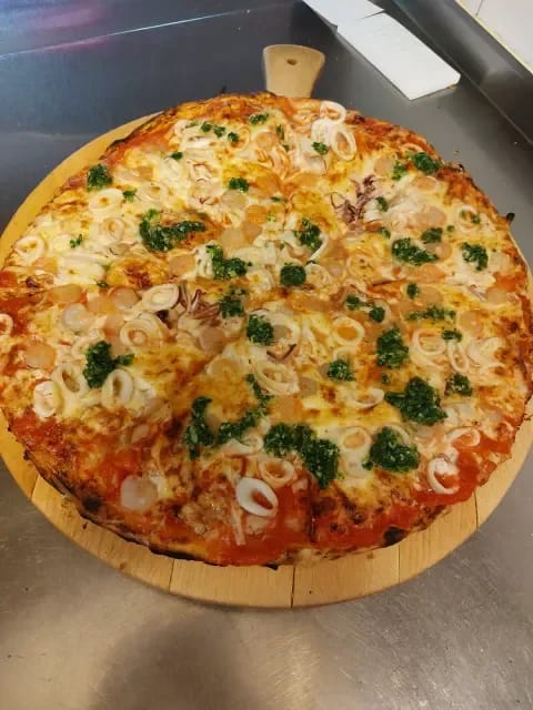 Pica z lignji, kozicami in zeleno tržaško omako na leseni deski.